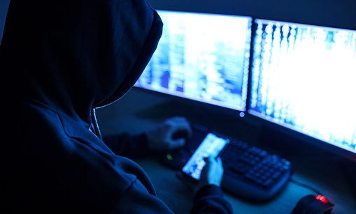Hacker tentando invadir sistemas com duas telas de computador