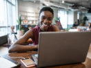 Mulher negra sorrindo em frente ao computador em mesa de escritório