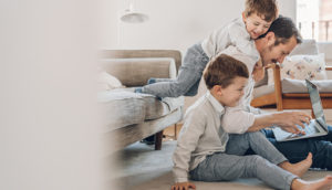 Pai tentando trabalhar no notebook com os filhos brincando com ele ao lado