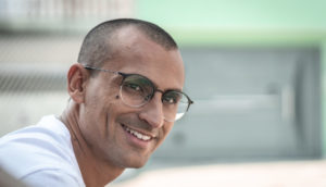 Edu Lyra, de óculos, no canto à esquerda olhando de lado e sorrindo