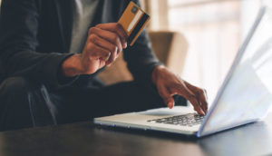 Mulher com laptop e cartão de crédito na mão, alusivo aos benefícios dos cartões de crédito Safra