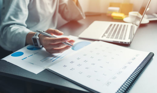 Pessoa com laptop, bloco de anotações e caneta para marcar eventos de números da agenda semanal