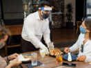 Garçom servindo duas pessoas em mesa de restaurante, negócio que foi um dos mais afetados do setor de serviços