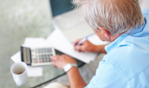 Pessoa sentada de costas fazendo contas com calculadora e a cartilha de educação financeira para idosos ao lado