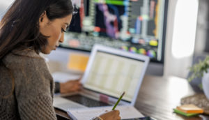 Mulher com laptop, monitor, lápis e calculadora olhando a carteira de dividendos
