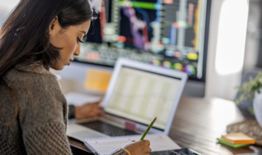 Mulher com laptop, monitor, lápis e calculadora olhando a carteira de dividendos