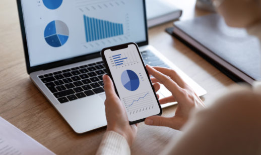 Mulher com celular nas mãos e laptop ao escolher um fundo de investimento