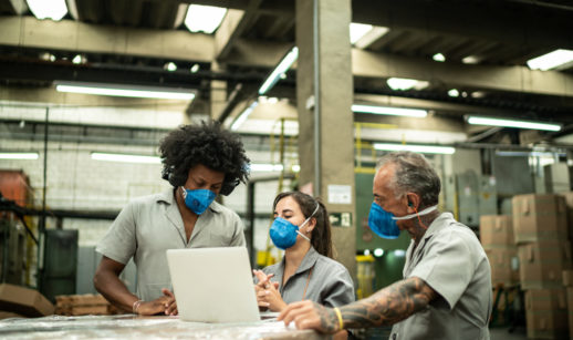Três funcionários de fábrica com máscaras trabalhando