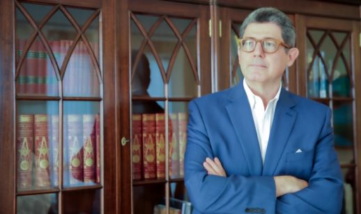 Joaquim Levy, de frente, com os braços cruzados e livros atrás