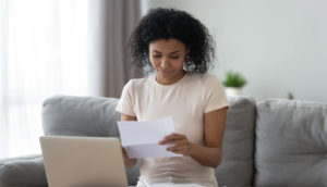 Mulher segurando recibos e notas para deduções no imposto de renda em frente ao computador