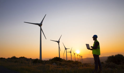 Trabalhador em campo de energia eólica e pôr do sol ao fundo