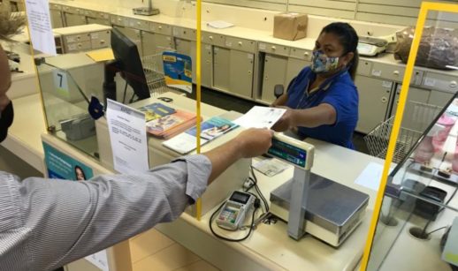 Atendente dos Correios recebendo carta de pessoa que pagará tarifa mais cara