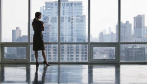 Executiva olhando por janela de sala de reuniões, pensando sobre os fatores de risco