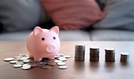 Cofre em forma de porco sobre mesa com moedas no entorno alusivo à poupança