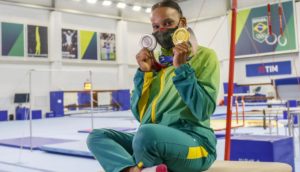 Rebeca Andrade, atleta do Flamengo, sentada em ginásio com suas duas medalhas de ouro e prata de Tóquio 2020