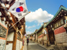 Bairro tradicional da Coreia do Sul com bandeira do país e céu azul com uma nuvem, alusivo à redução de emissões de carbono que o país pretende