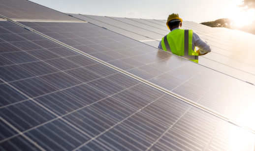 Painéis de energia solar iluminados com trabalhador de colete amarelo e capacete laranja no meio, alusivo à atividade da EDP