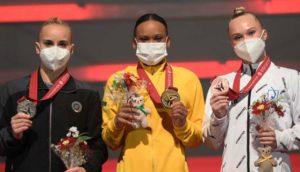 Rebeca Andrade no meio de pódio com duas ginastas ao lado, recebendo o ouro