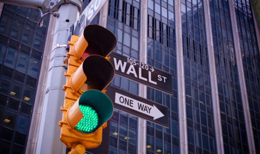 Semáforo com sinal verde em primeiro plano e placa com direções para Wall Street, alusivo aos BDRs para investir em novembro