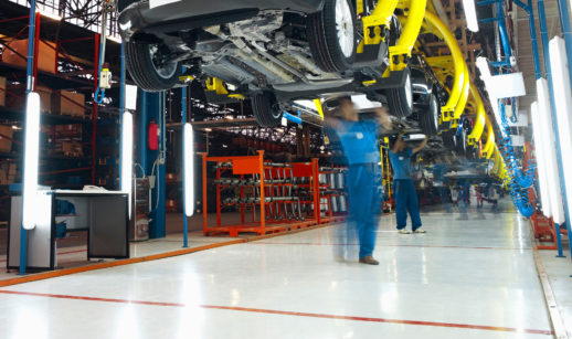 Linha de produção de veículos, com automóveis suspensos e funcionários de macacão azul em baixo