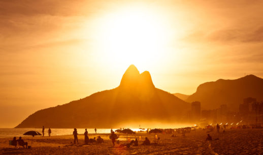 Praia de Ipanema, no Rio de Janeiro, com o Morro Dois Irmãos ao fundo, com sol raiando, alusivo à prevenção ao câncer de pele