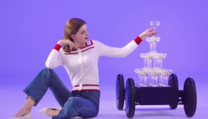 Mulher sentada no chão pegando taça de uma pilha colocada sobre o MobED, novo robô da Hyundai