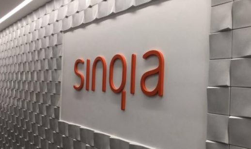 Letreiro escrito "Sinqia" em laranja em parede branca atrás