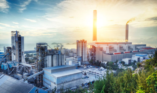 Paisagem de indústria petroquímica com verde de árvores ao lado e pôr do sol ao fundo, alusivo à compensação de carbono
