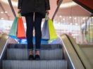 Close de pessoa subindo a escada rolante com sacolas nas mãos, alusivo aos shoppings centers da Multiplan