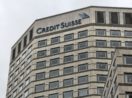 Fachada vista de baixo para cima de prédio do Credit Suisse com céu nublado ao fundo