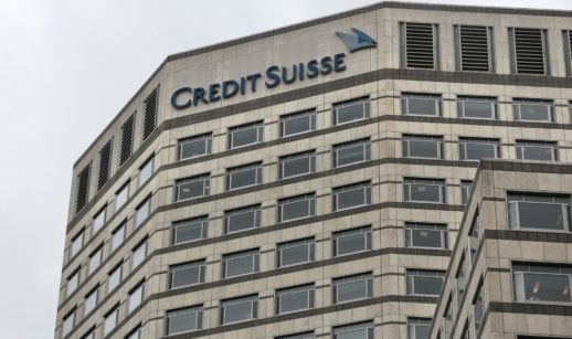 Fachada vista de baixo para cima de prédio do Credit Suisse com céu nublado ao fundo