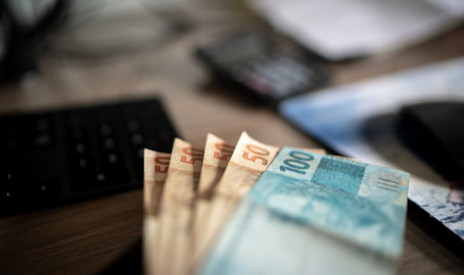 Notas de cem e cinquenta reais enfileiradas sobre mesa com calculadora e PC ao fundo, alusivo aos pedidos de transferência via sistema Valores a Receber, do Banco Central