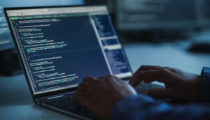 Close de laptop com tela de dados aberta e mãos de pessoa teclando no escuro, alusivo a um ataque hacker