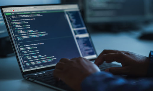 Close de laptop com tela de dados aberta e mãos de pessoa teclando no escuro, alusivo a um ataque hacker