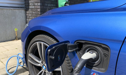 Close de mangueira de abastecimento de carros elétricos plugada à uma BMW azul marinho