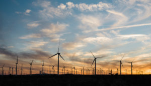 Parque de energia eólica em pôr do sol, com silhuetas das hélices dos geradores, alusivo ao novo empreendimento da BRF e da AES Brasil no Nordeste