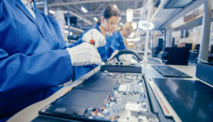 Linha de produção de produtos eletrônicos com funcionários em macacão azul, alusivo aos chips necessários à indústria