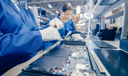 Linha de produção de produtos eletrônicos com funcionários em macacão azul, alusivo aos chips necessários à indústria