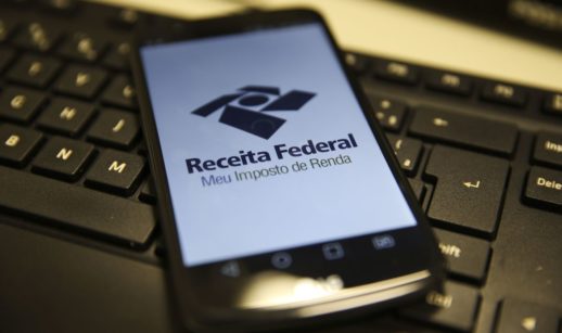 Close de celular com a tela do aplicativo Meu Imposto de Renda aberta sobre teclado preto, alusivo à incidência do IR sobre os investimentos