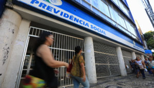 Fachada do INSS, com pessoas caminhando à frente, alusivo ao atendimento presencial que será retomado