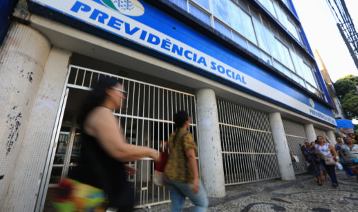 Fachada do INSS, com pessoas caminhando à frente, alusivo ao atendimento presencial que será retomado