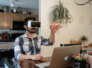 Homem de camisa xadrez azul com óculos de realidade virtual com laptop à frente, alusivo ao metaverso