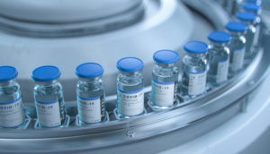 Frascos de vacinas contra a covid-19 enfileirados em máquina metálica, alusivo à Pfizer e à Moderna