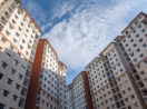 Perspectiva de baixo para cima de prédios residenciais com céu azul e nuvens brancas acima, alusivo às vendas e lançamentos de imóveis no Brasil