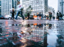 Perspectiva de baixo para cima de calçada molhada em São Paulo com pessoas caminhando e prédios ao fundo, alusivo ao desemprego no Brasil