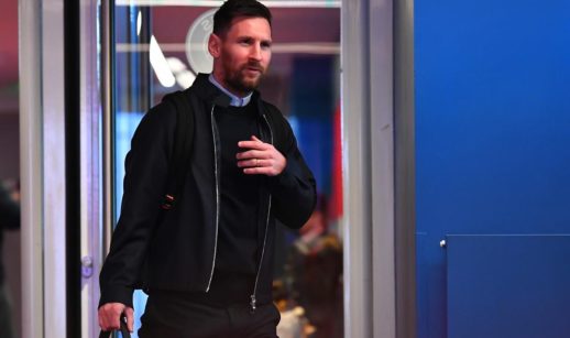 Lionel Messi, embaixador da Socios.com, de jaqueta, suéter e mala na mão, sorrindo com a boca fechada
