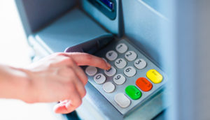 Close de mão clicando caixa eletrônico de bancos, alusivo ao setor financeiro