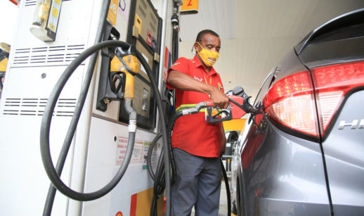Detalhe de frentista enchendo tanque de carro com bomba de combustível, alusivo à redução do ICMS