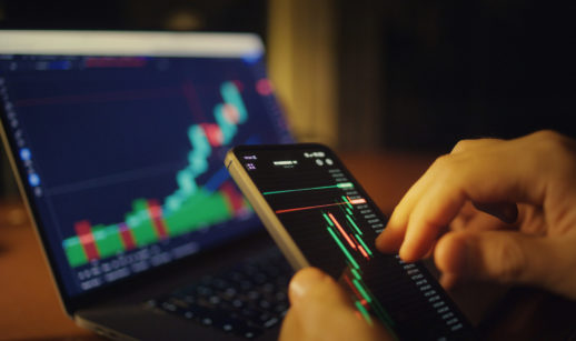 Mãos com telas de mercado financeiro, alusivo aos investimentos com alta da Selic