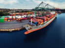 Aérea de porto com destaque para navio cargueiro com contêineres, alusivo às commodities